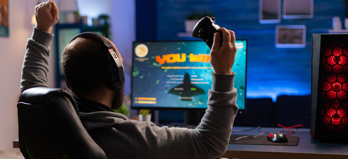 Winner gamer sitting on gaming chair at desk and playing space shooter video games with controller.