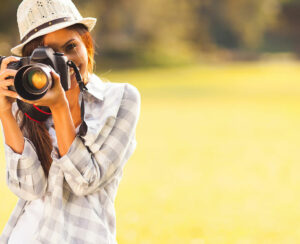 smiling young woman using a camera to take photo outdoors at the park