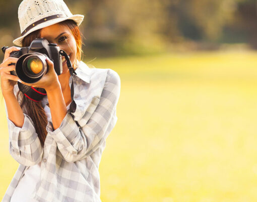 smiling young woman using a camera to take photo outdoors at the park