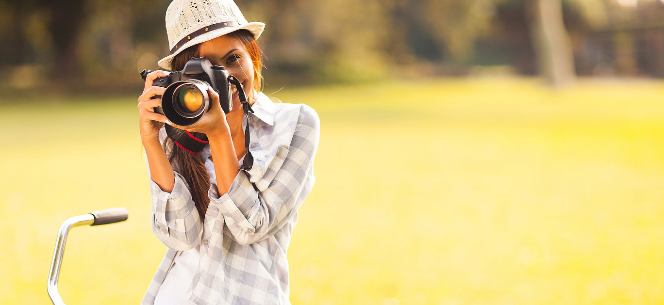 smiling young woman using a camera to take photo outdoors at the park