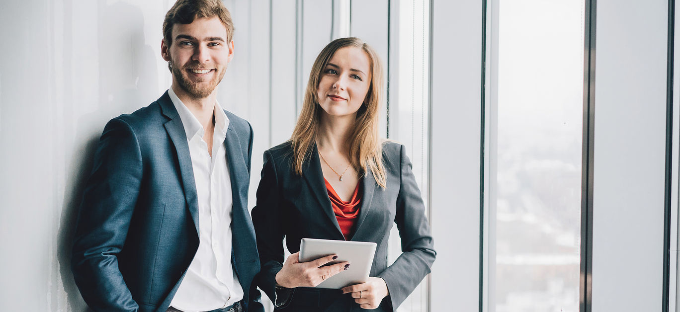 Group of business people a man in a suit and a woman in a red dress and jacket holding a tablet winter city landscape outside the window on the background