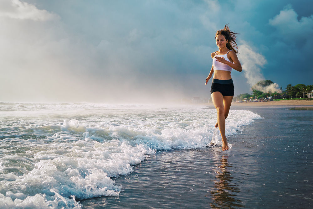 Active sporty woman run along ocean surf by water pool to keep fit and health