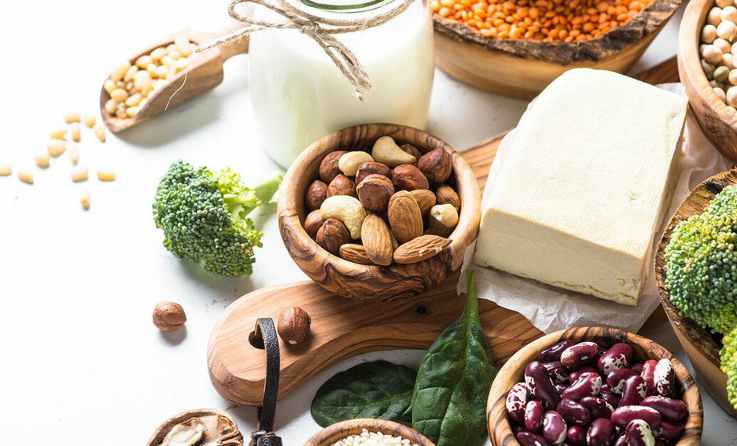 Vegan protein source. Tofu, vegan milk, beans, lentils, nuts, broccoli spinach and seeds on white table with copy space. Healthy balanced vegetarian food.