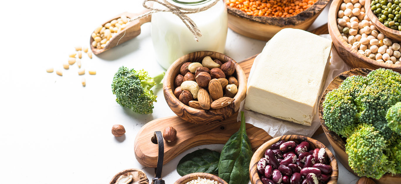 Vegan protein source. Tofu, vegan milk, beans, lentils, nuts, broccoli spinach and seeds on white table with copy space. Healthy balanced vegetarian food.