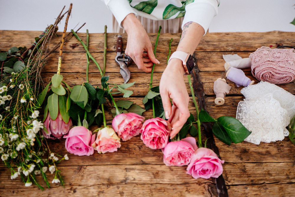 A girl florist makes a bouquet in a light studio on a wooden table.