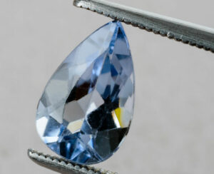 Fine blue drop shaped blue beryl aquamarine gemstone held by tweezers.