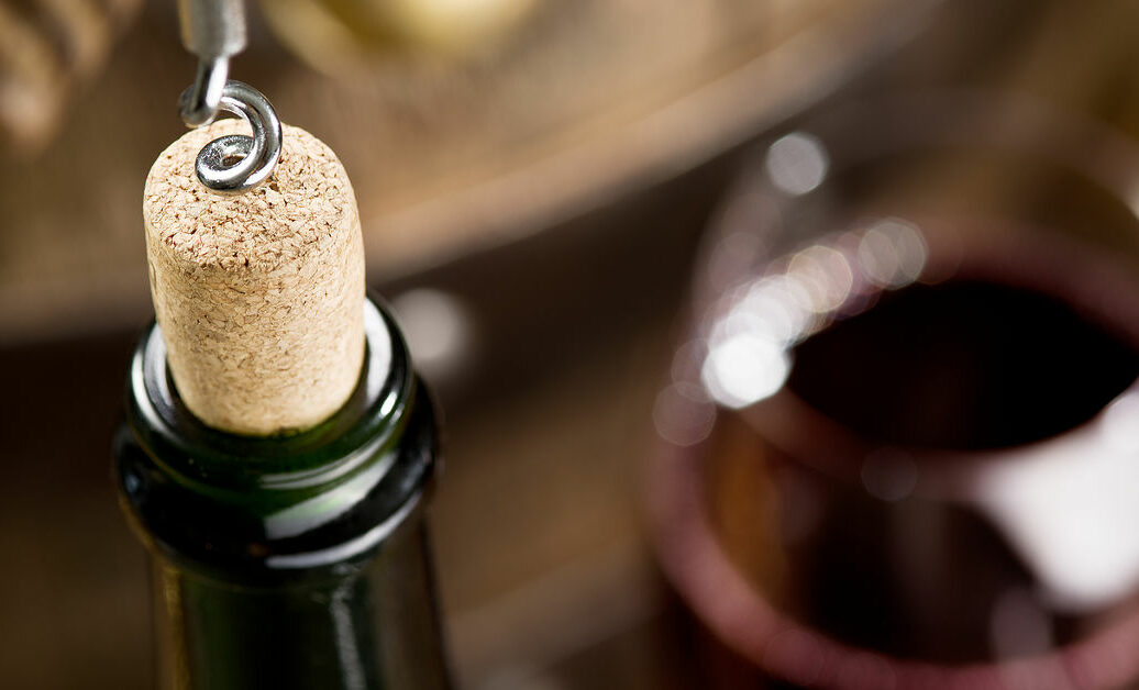 Opening of a wine bottle with corkscrew with wooden barrel on the background.