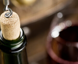 Opening of a wine bottle with corkscrew with wooden barrel on the background.