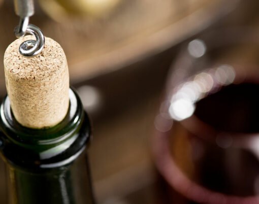 Opening of a wine bottle with corkscrew with wooden barrel on the background.