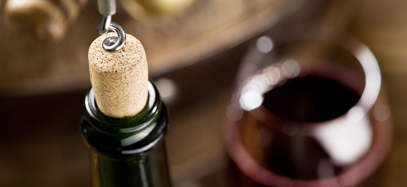 Opening of a wine bottle with corkscrew with wooden barrel on the background.