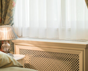 Wooden cover for radiator near window in home interior