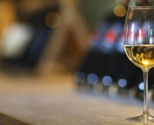 Wine bottles on a wooden shelf. Wine bar. Close up on glass of white wine