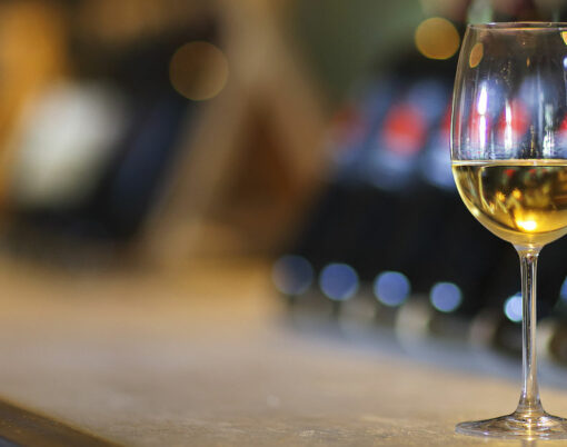 Wine bottles on a wooden shelf. Wine bar. Close up on glass of white wine