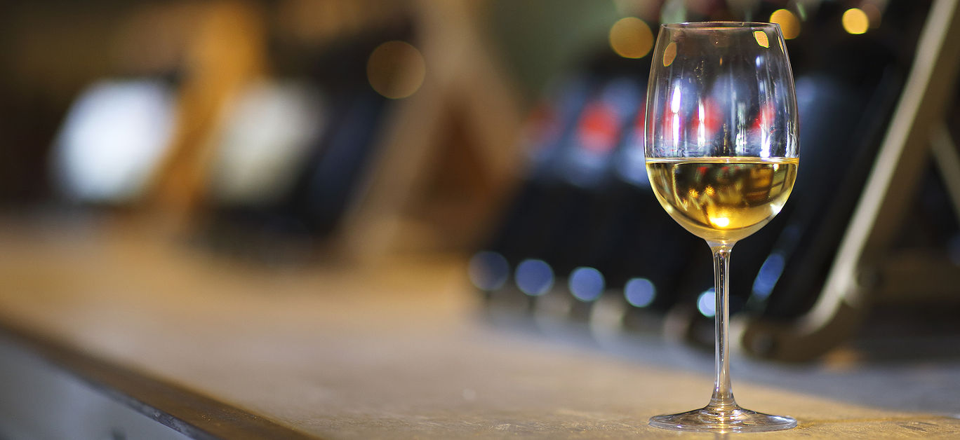 Wine bottles on a wooden shelf. Wine bar. Close up on glass of white wine