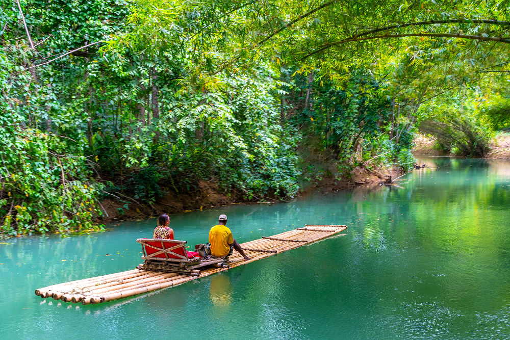 Female tourist and tour guide sit on bamboo raft on Martha Brae River in Falmouth, Jamaica