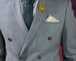 Man in double breasted grey suit plaid texture blue necktie flower brooch and dot pattern handkerchief close up