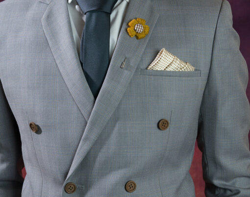 Man in double breasted grey suit plaid texture blue necktie flower brooch and dot pattern handkerchief close up