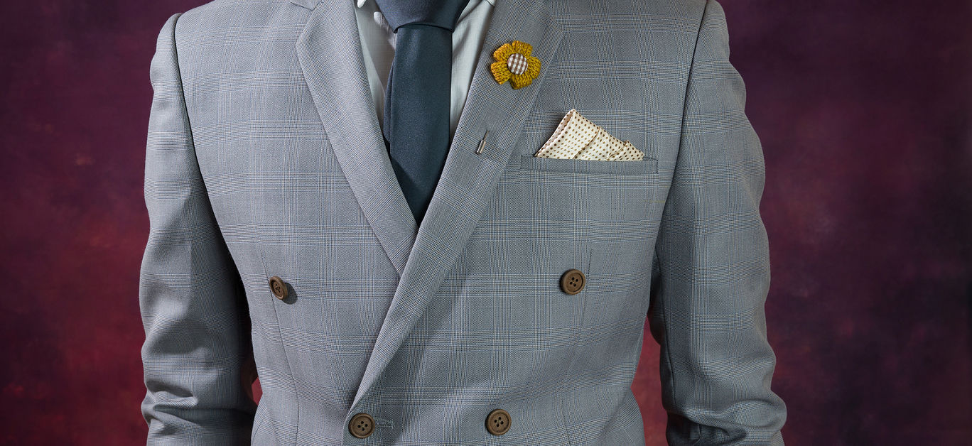 Man in double breasted grey suit plaid texture blue necktie flower brooch and dot pattern handkerchief close up