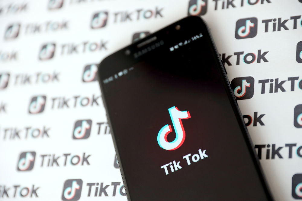 Tik Tok smartphone app on screen and Many TikTok logo printed on paper