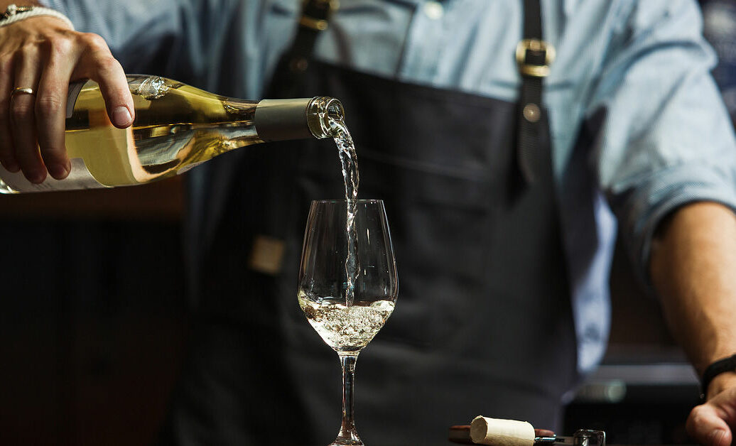 Male sommelier pouring white wine into long-stemmed wineglasses