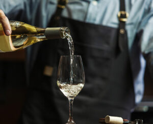 Male sommelier pouring white wine into long-stemmed wineglasses