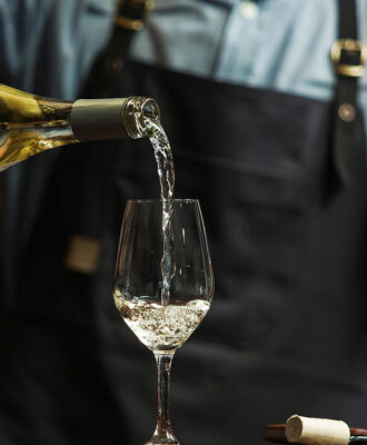 Male sommelier pouring white wine into long-stemmed wineglasses