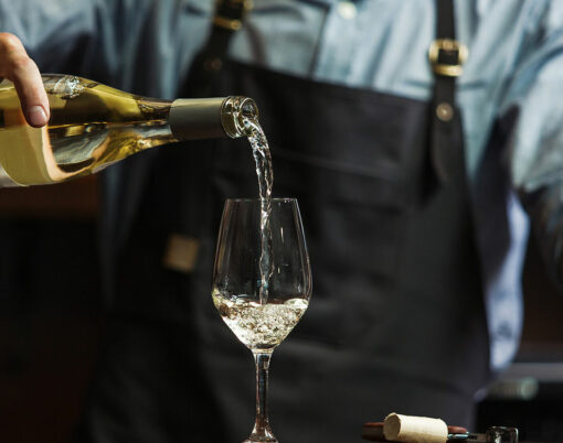 Male sommelier pouring white wine into long-stemmed wineglasses