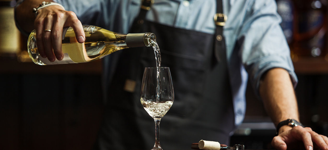 Male sommelier pouring white wine into long-stemmed wineglasses