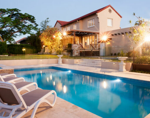 Luxury house and swimming pool decoration at an evening with flashing lights around the garden with trees there is a green lawn around the waterside with chairs