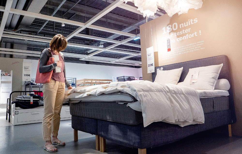 Elegant French woman looking at bed duvet choosing furniture and bed linen mattress