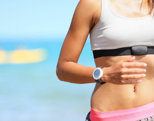 Runner woman with heart rate monitor running on beach with watch and sports bra top. Beautiful fit female fitness model training and working out outside in summer at part of healthy lifestyle.