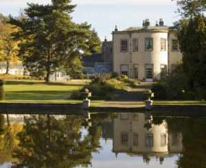 reflection of stately home in own grounds on small lake surrounded by trees