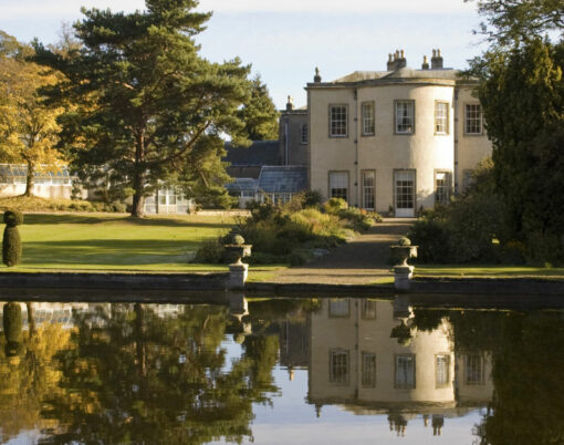 reflection of stately home in own grounds on small lake surrounded by trees